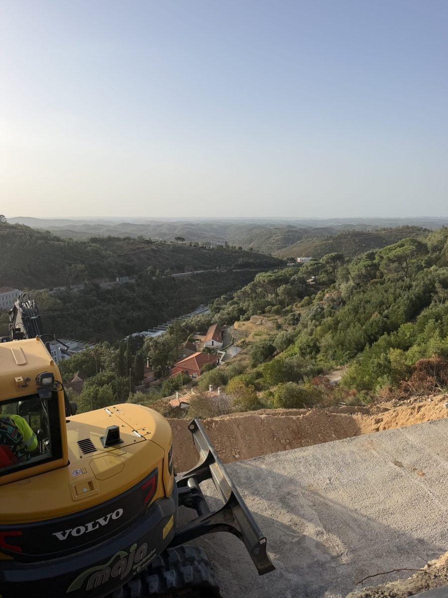 View down a wooded valley of the Monchique hills from a hillside road works site, with a yellow digger in the foreground