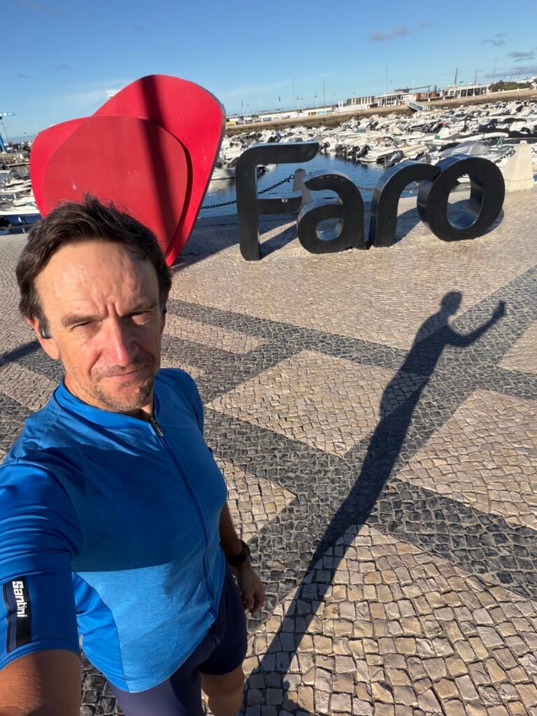 Richard in a sky-blue Maglia Azzurra jersey taking a selfie beside the big Faro sign by the marina