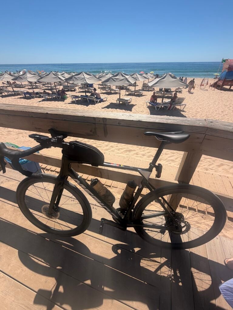 Black road bike leaning against the boardwalk rail above the beach at Alvor, with parasols stretching down to the sea