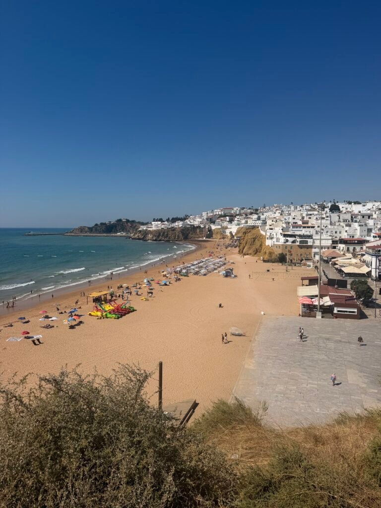 The beach at Albufeira seen from the clifftop, busy with sunbathers, with the white town beyond