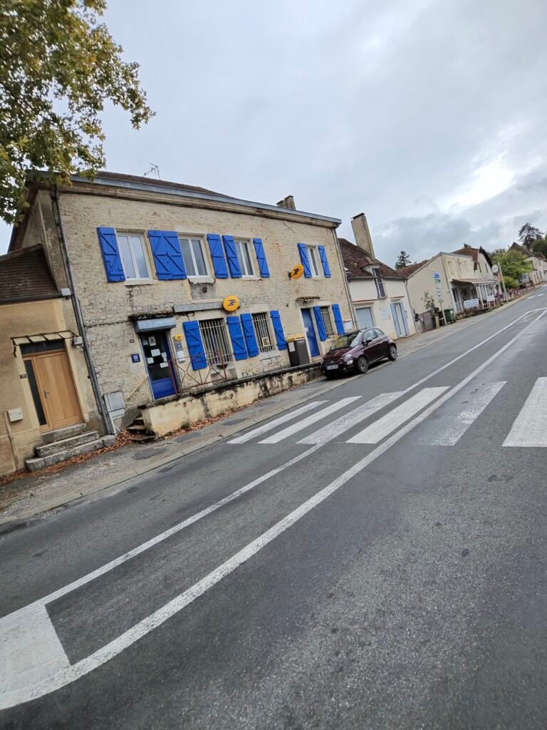 A building with blue shutters on the main road through Payrac