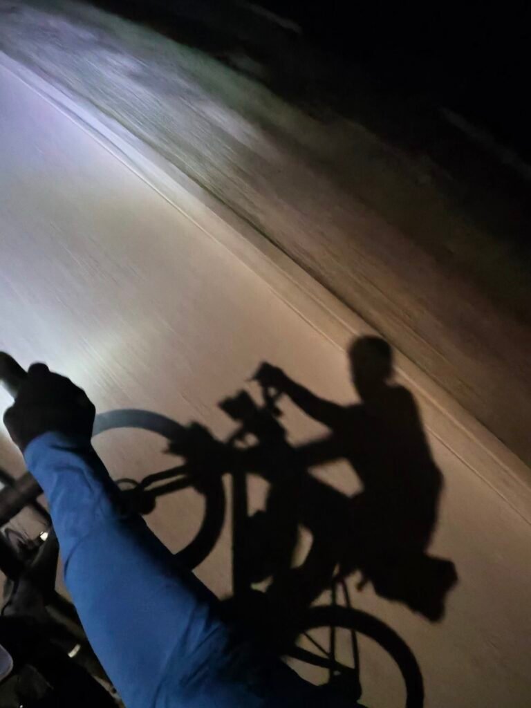 The shadow of rider and bike thrown up the road by a car’s headlights from behind, in Cahors