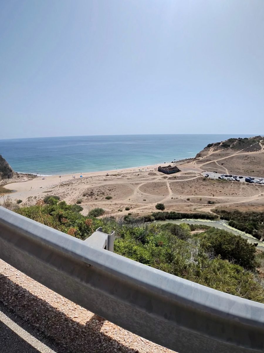 View from the road over a crash barrier down to a sandy beach and headland on the way into Lagos