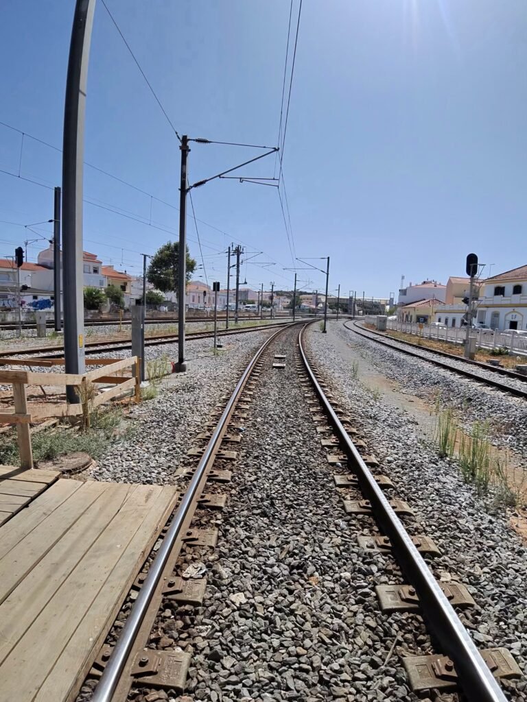 Looking along a single railway track from a level crossing on the way to Loulé, with signals and white buildings in the distance