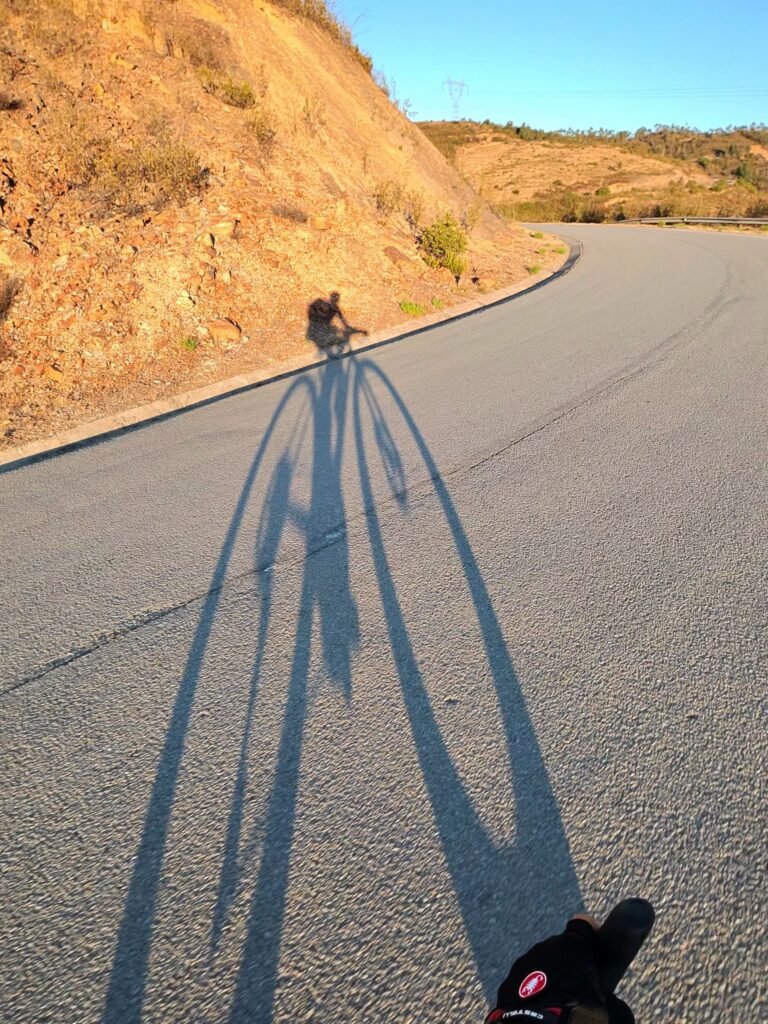 Rider and bike casting a long early-morning shadow on the road climbing towards Alferce