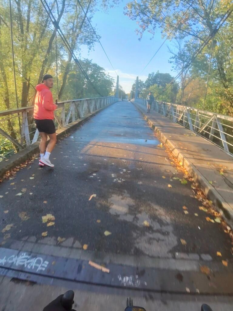 Crossing the Pont de Fil suspension footbridge over the Loire in Tours in low morning sun, a runner by the rail