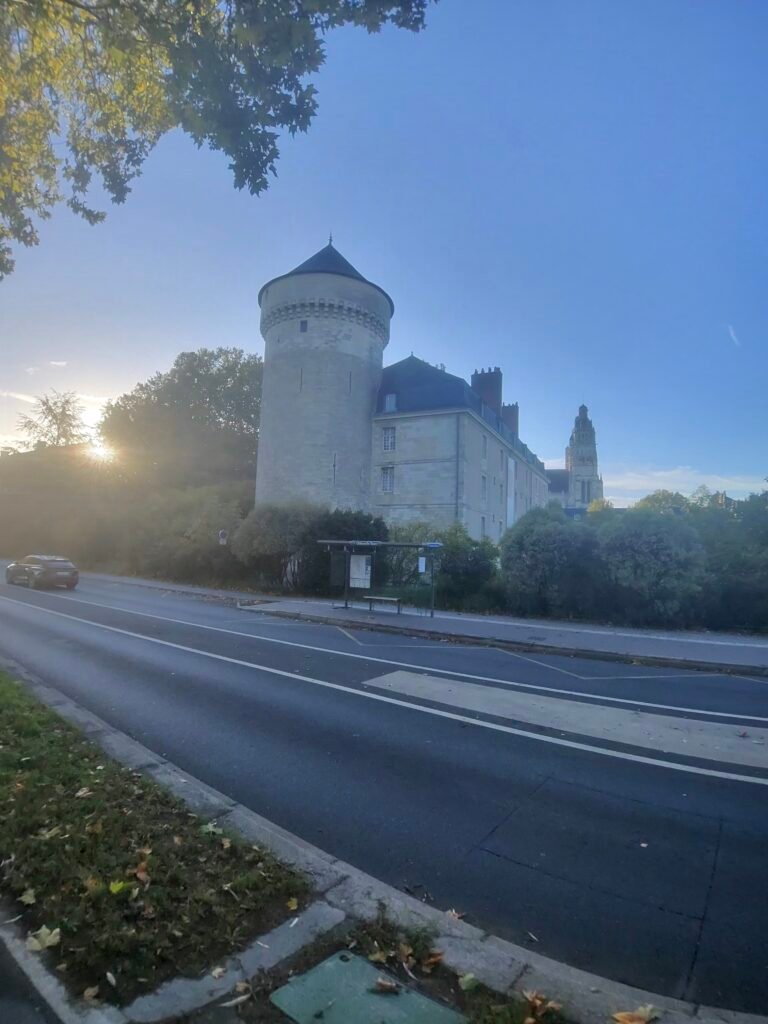 The round tower of the Château de Tours beside the riverside road, with the sun low behind the trees