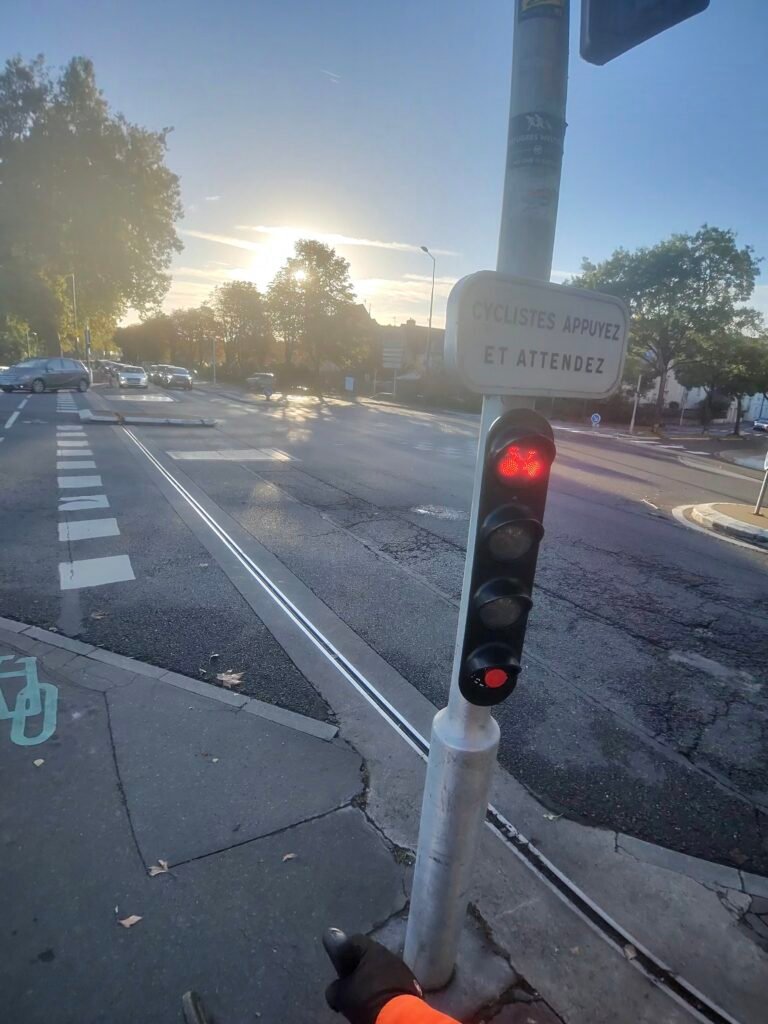 A gloved hand on a cyclists’ traffic light showing red in Tours, its sign asking cyclists to press and wait
