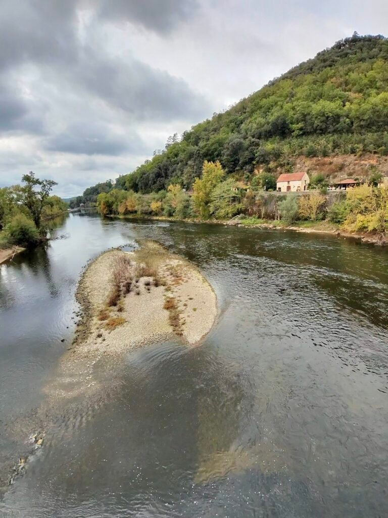 A sandy islet in the Dordogne below wooded hills, under a cloudy sky