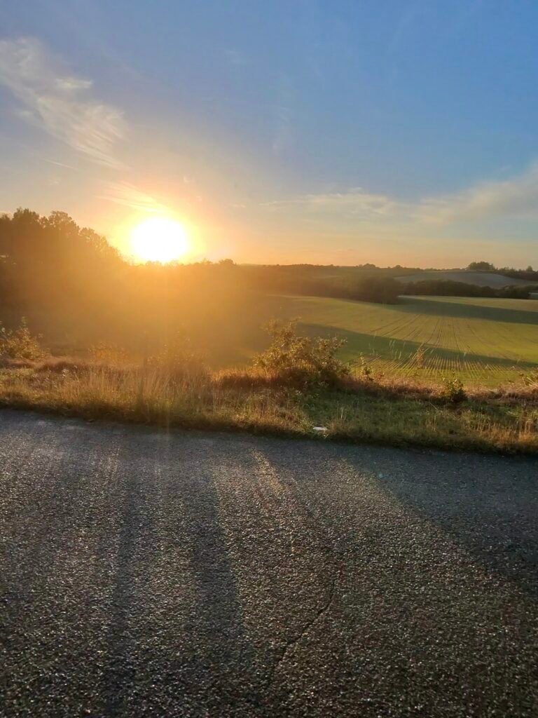 The sun setting low over fields beside a country road in the Quercy